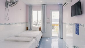 Une chambre d’hôtel équipée d’un lit, d’un ventilateur fixé au mur, d’un climatiseur, d’une télévision et offrant une vue sur la ville par la fenêtre.