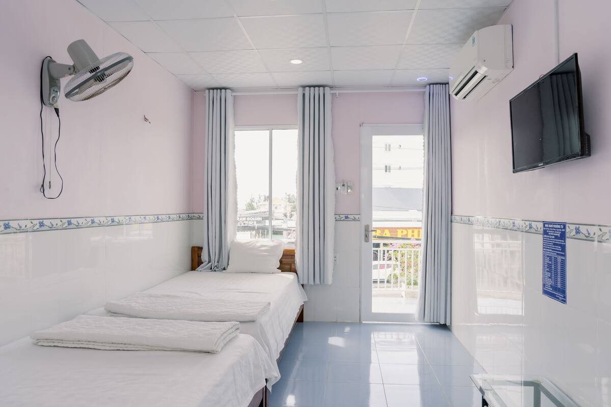 Une chambre d’hôtel équipée d’un lit, d’un ventilateur fixé au mur, d’un climatiseur, d’une télévision et offrant une vue sur la ville par la fenêtre.