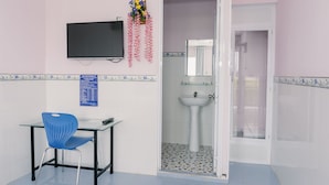 Une pièce avec une chaise bleue, un téléviseur à écran plat, une petite table, un lavabo et une porte donnant sur une autre pièce.