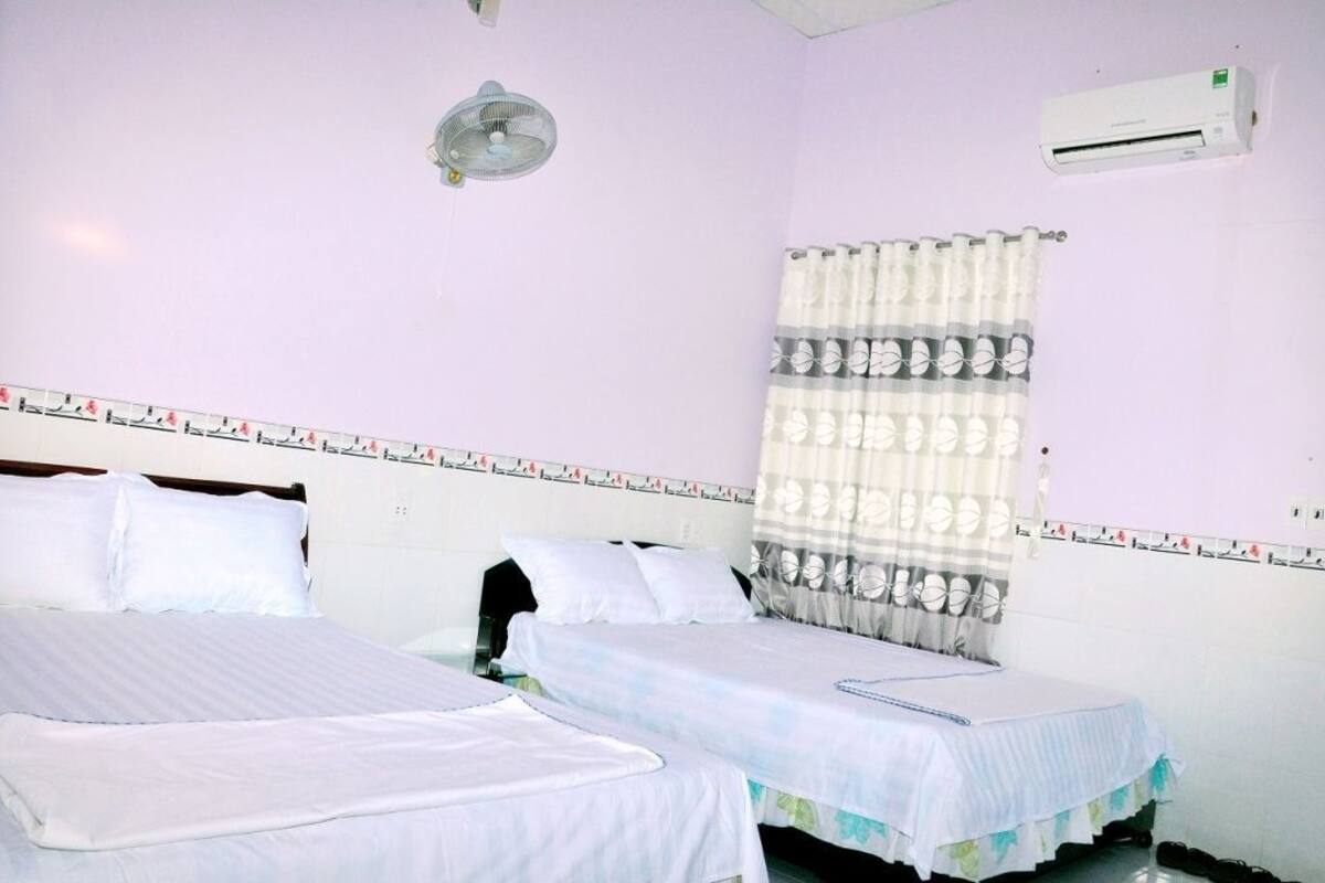 Une chambre d’hôtel avec deux lits, un ventilateur de plafond, un appareil de climatisation et une fenêtre avec un rideau à motifs.