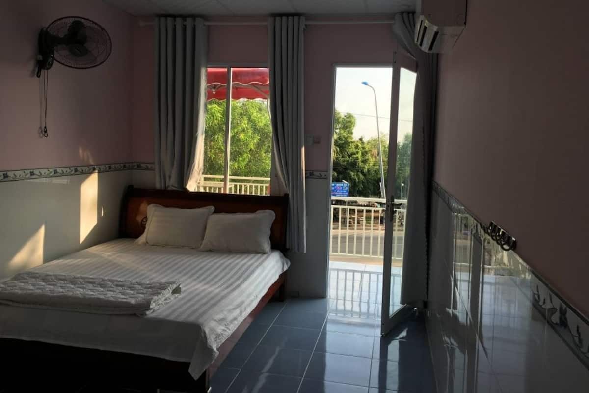 Une chambre d’hôtel avec un lit, un ventilateur, une fenêtre avec des rideaux et une vue sur l’extérieur.