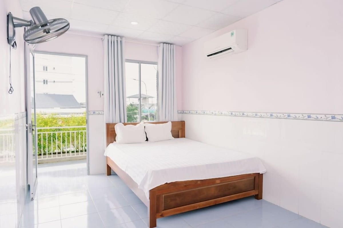 A bedroom with a bed, a ceiling fan, an air conditioning unit, and a view of the outside.