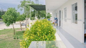 Une chambre d’hôtel avec un balcon, donnant sur la rue, et un espace jardin agrémenté de fleurs jaunes.
