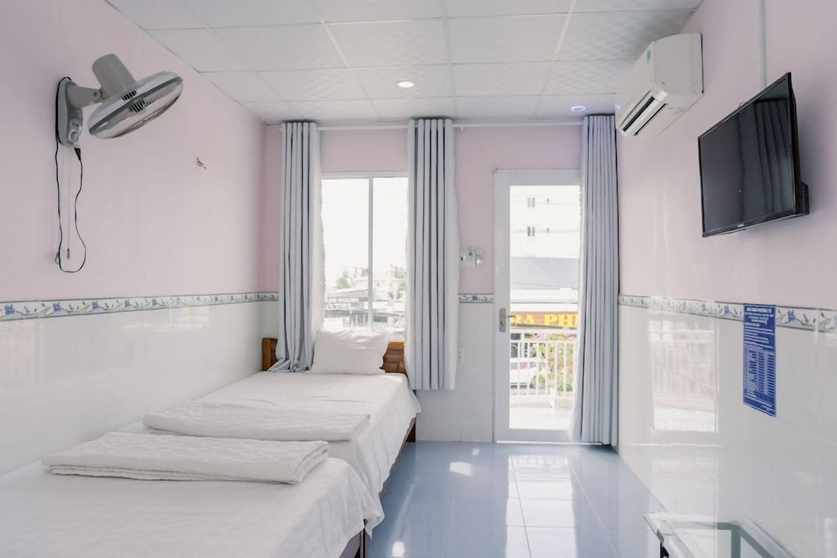 A hotel room with a bed, a desk, a chair, a TV, and a window with curtains.