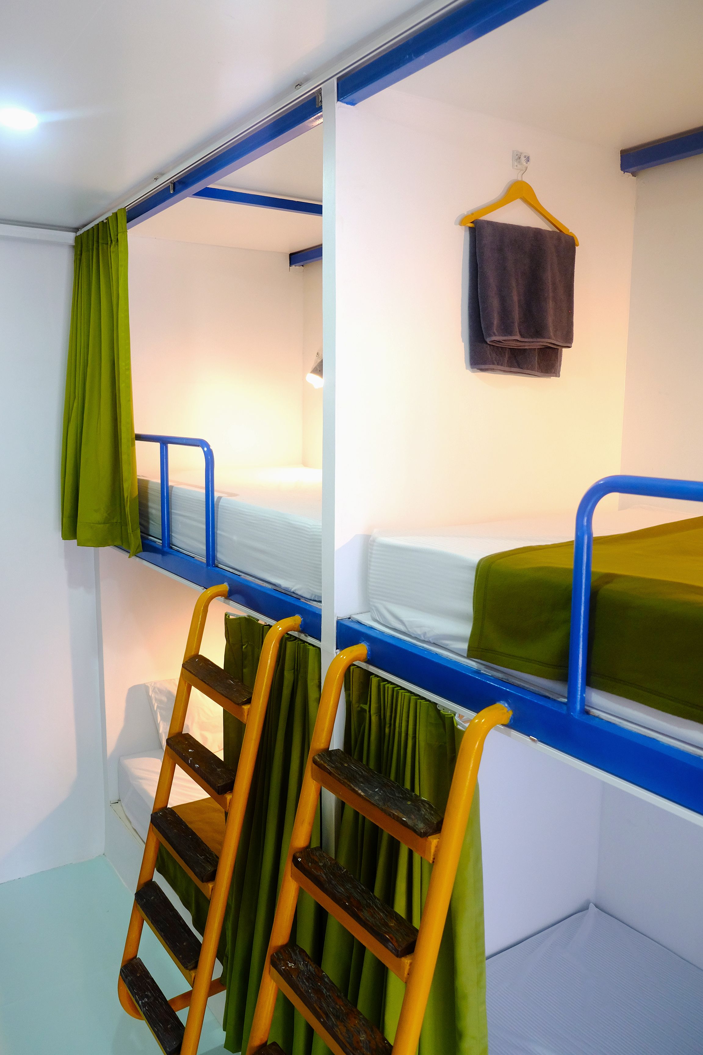 Une chambre avec un lit superposé, une échelle, des rideaux verts et une serviette accrochée au mur.