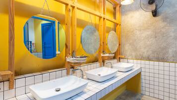 A bathroom with three sinks, a mirror, and a fan.
