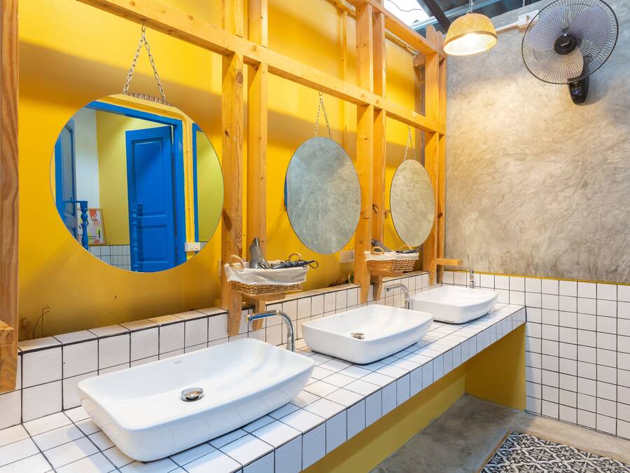 A bathroom with three sinks, a mirror, and a fan.