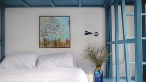 Ein Schlafzimmer mit Bett, einem Gemälde, einer Lampe und einer Blumenvase.