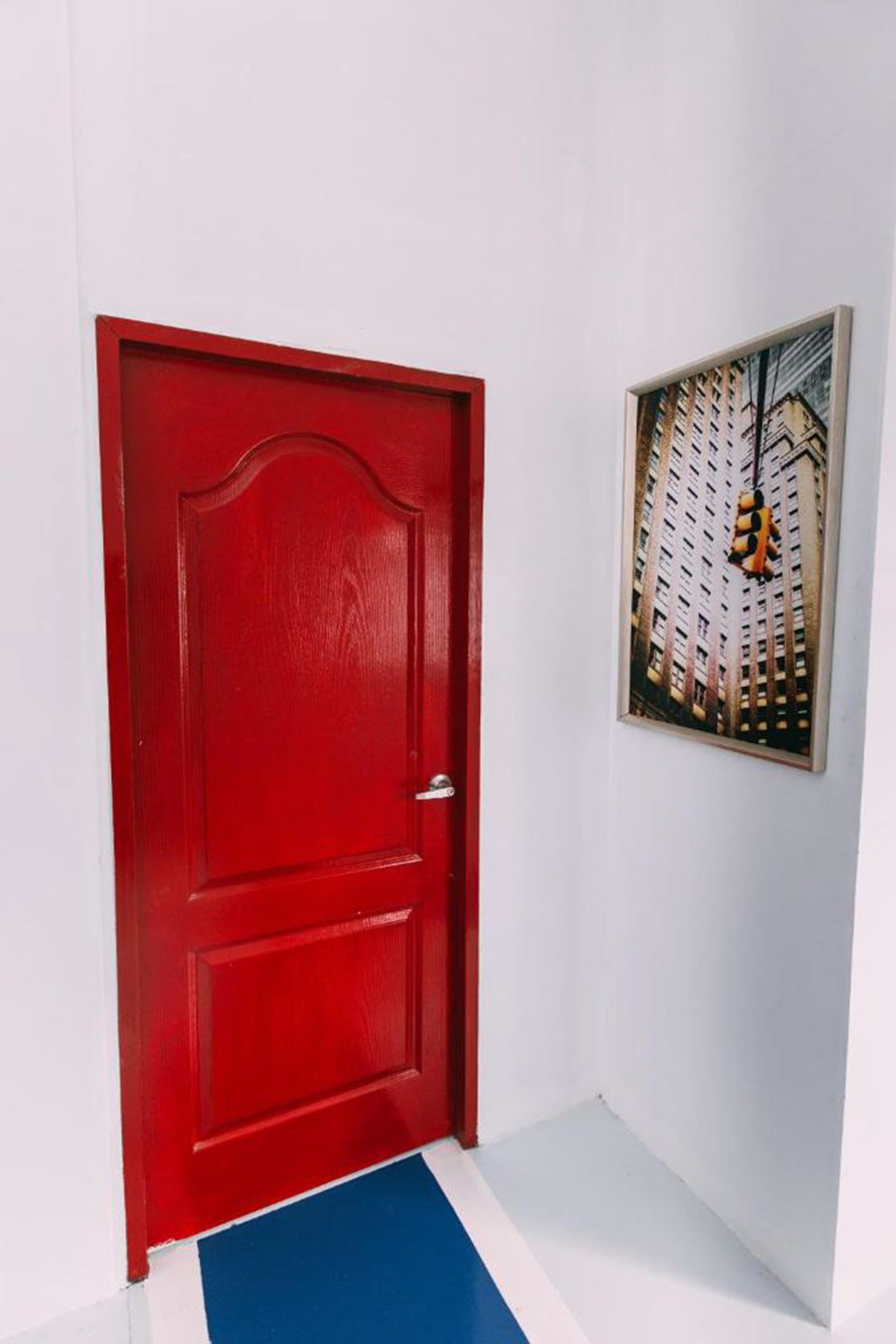 A red door with a white wall and a framed picture of a building.