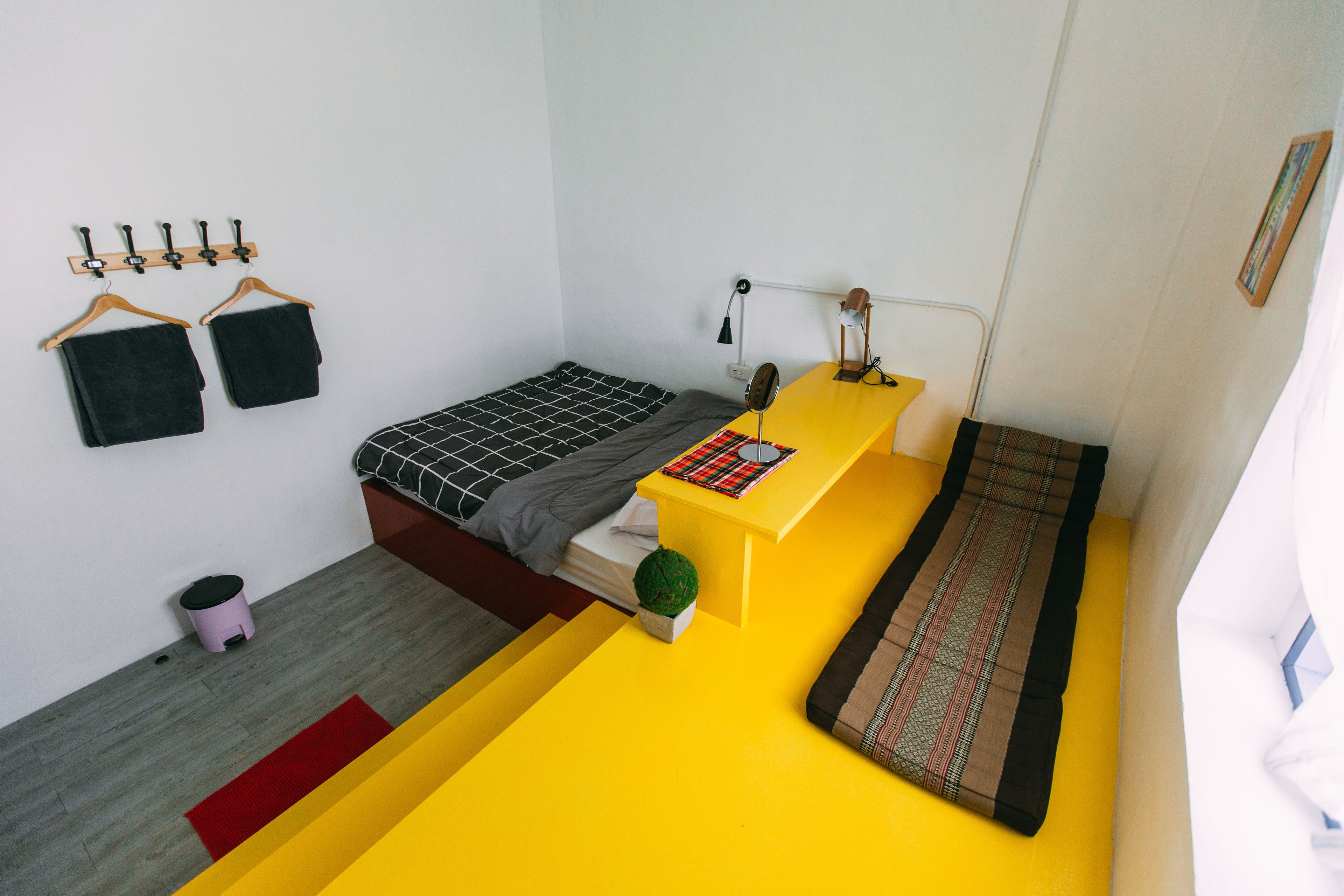 Una habitación pequeña con cama, un escritorio, un taburete y un perchero en la pared.