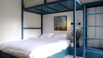 Un letto a castello con materasso bianco e struttura blu, un quadro al muro e un piccolo vaso con fiori.