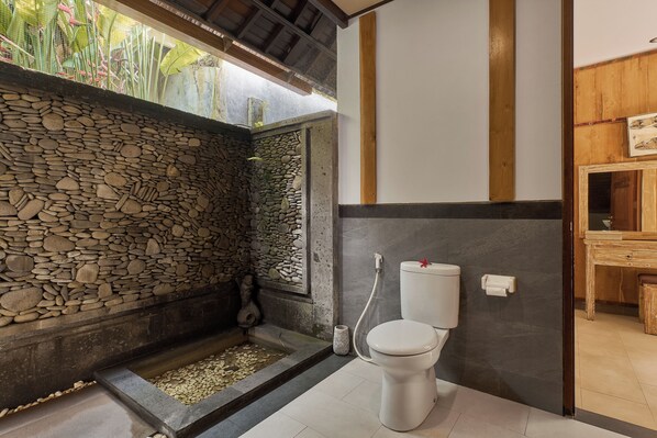 A bathroom with a stone wall, a toilet, and a shower area.