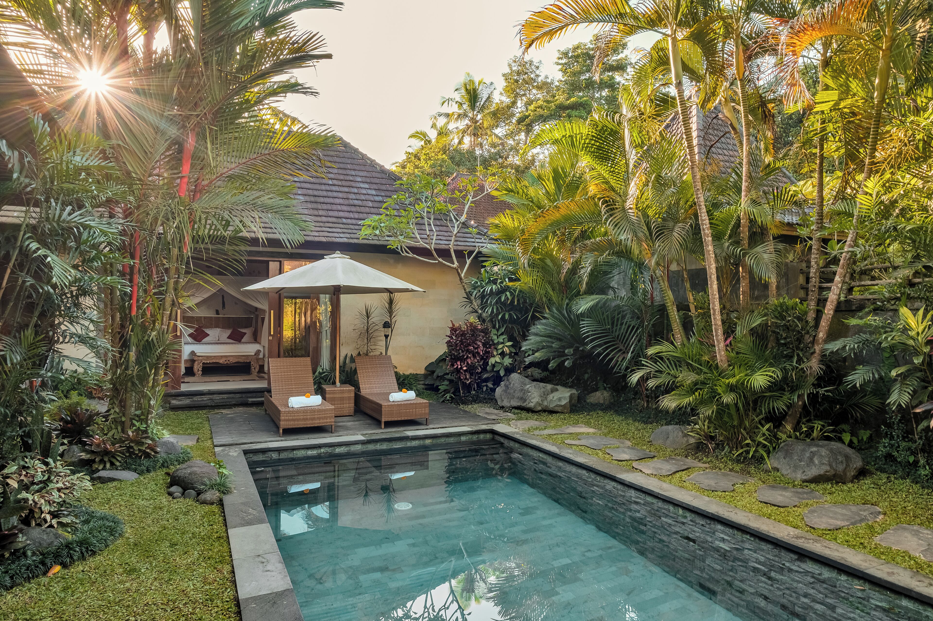 Un espace piscine doté de chaises longues et d’un coin salon abrité, le tout entouré de plantes tropicales.