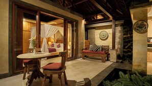 Un rincón exterior acogedor con una mesa redonda y sillas, un banco acolchado y un muro de piedra con un plato decorativo.