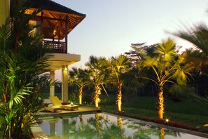 A pool area with lounge chairs, palm trees, and a building with a thatched roof. - Warisan Ubud Villa (Tegallalang)