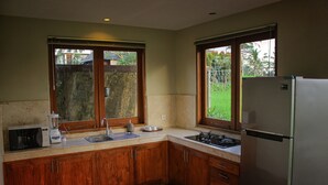A kitchen with wooden cabinets, a refrigerator, a microwave, a sink, and two windows. - Warisan Ubud Villa (Tegallalang)