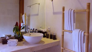 A bathroom with a large white sink, a mirror, a towel rack, and toiletries on the counter. - Warisan Ubud Villa (Tegallalang)