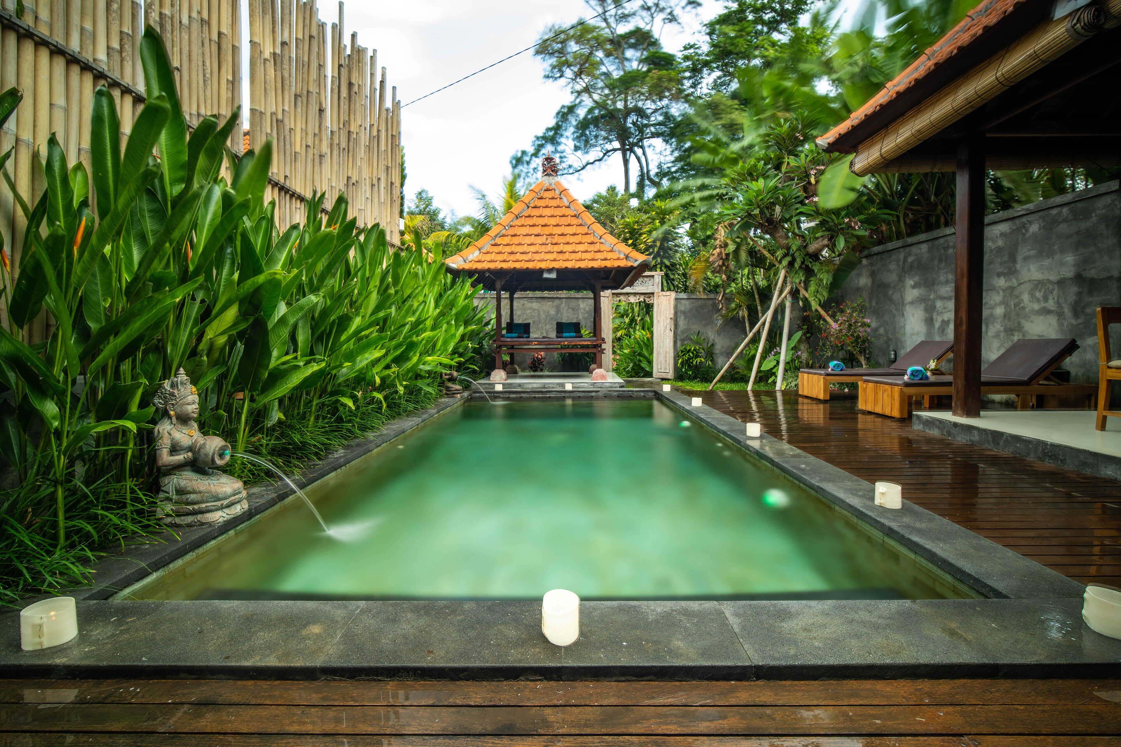 A serene pool area with a statue, a small pavilion, and wooden deck seating.