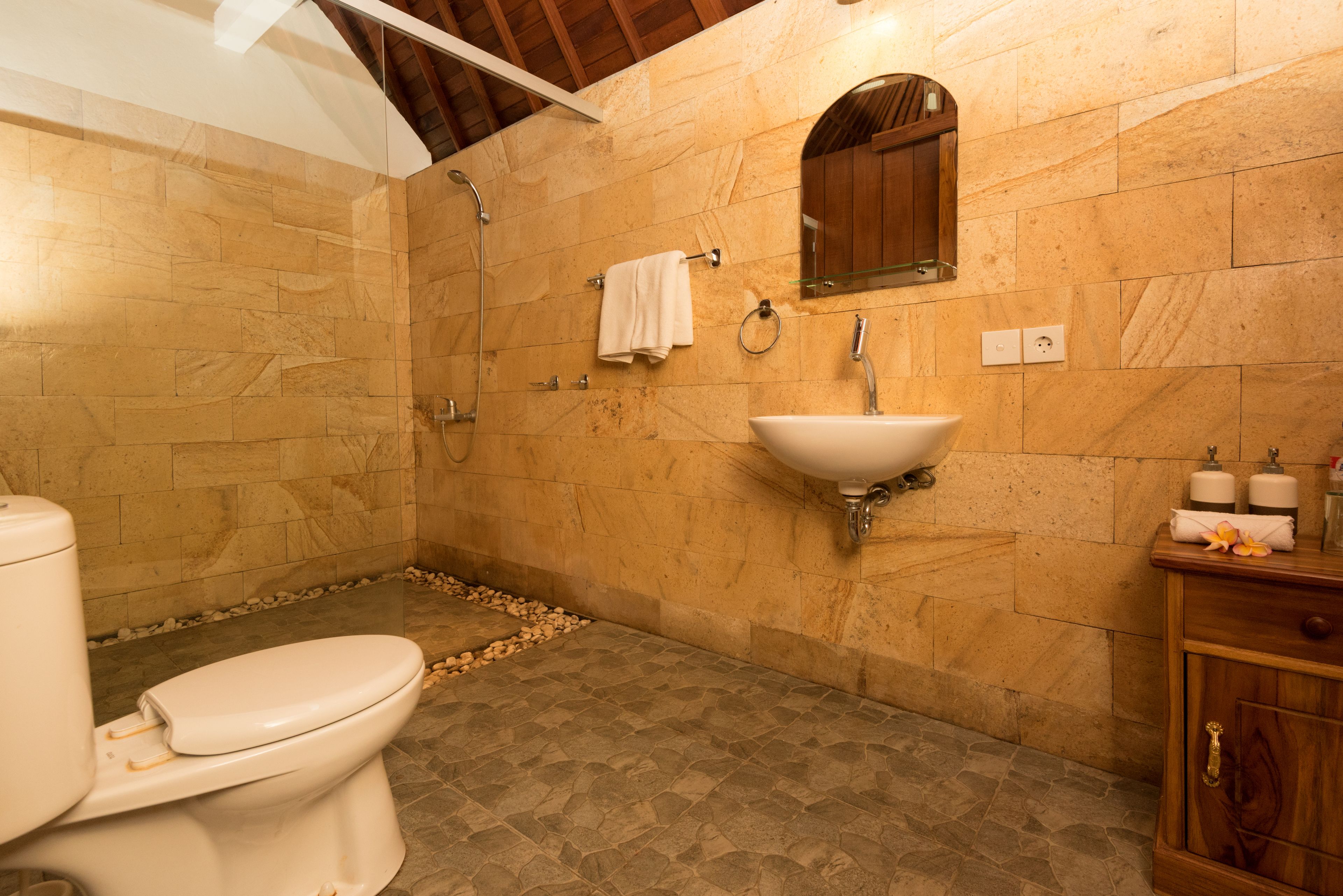 A bathroom with a toilet, sink, shower, and wooden cabinet.