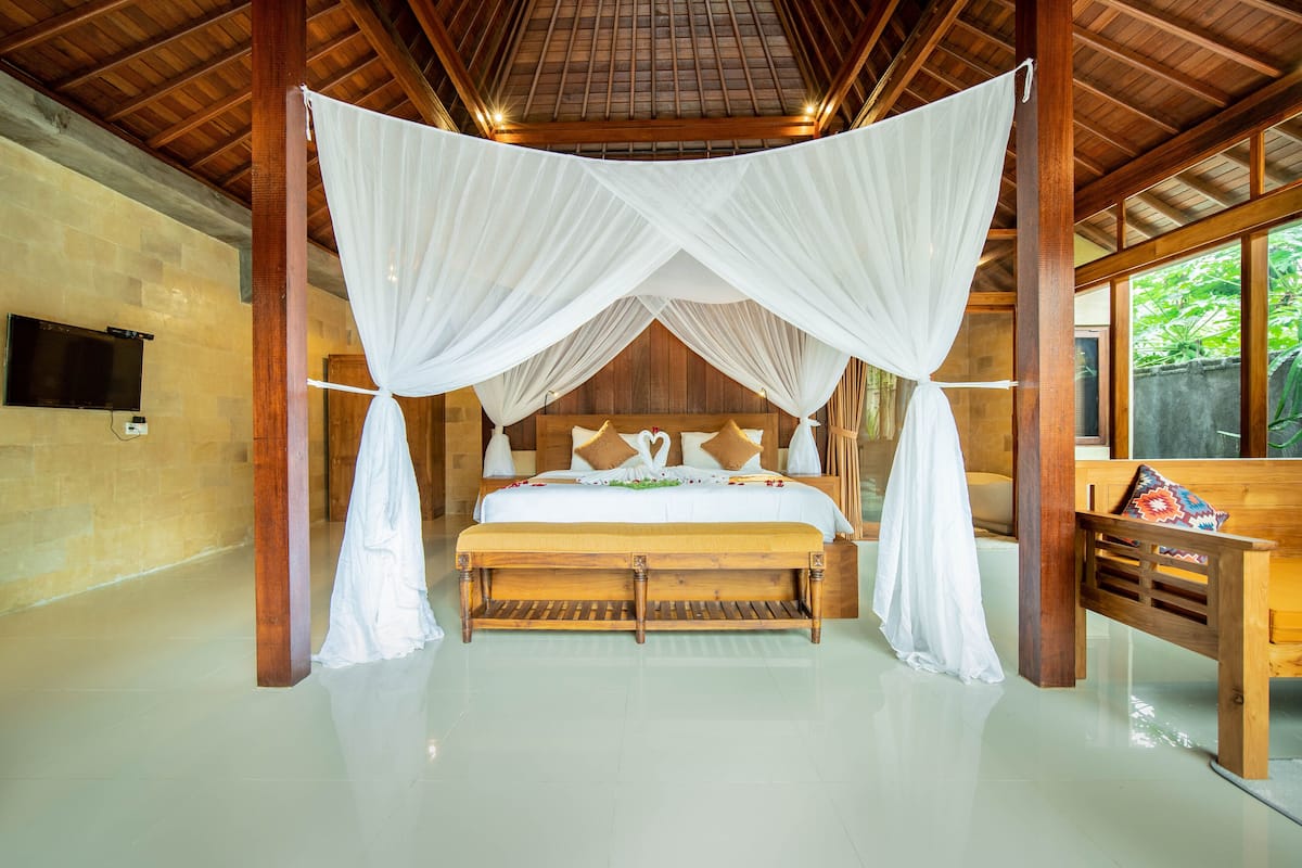 A spacious bedroom with a large bed, wooden headboard, and a bench with a colorful cushion.