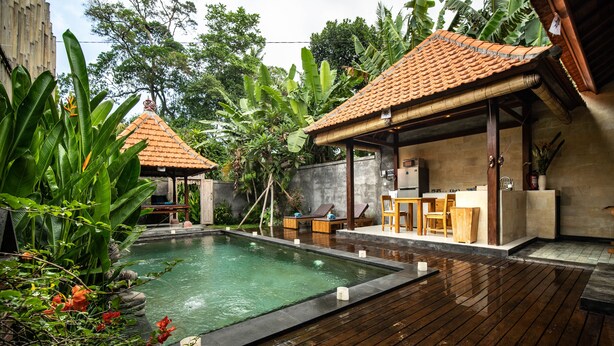 A wooden deck with a pool, outdoor seating, and a covered area with a tiled roof. - Naja Private Villa (Ubud)