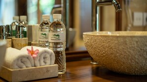 A bathroom with a stone sink, toiletries, and towels. - Naja Private Villa (Ubud)