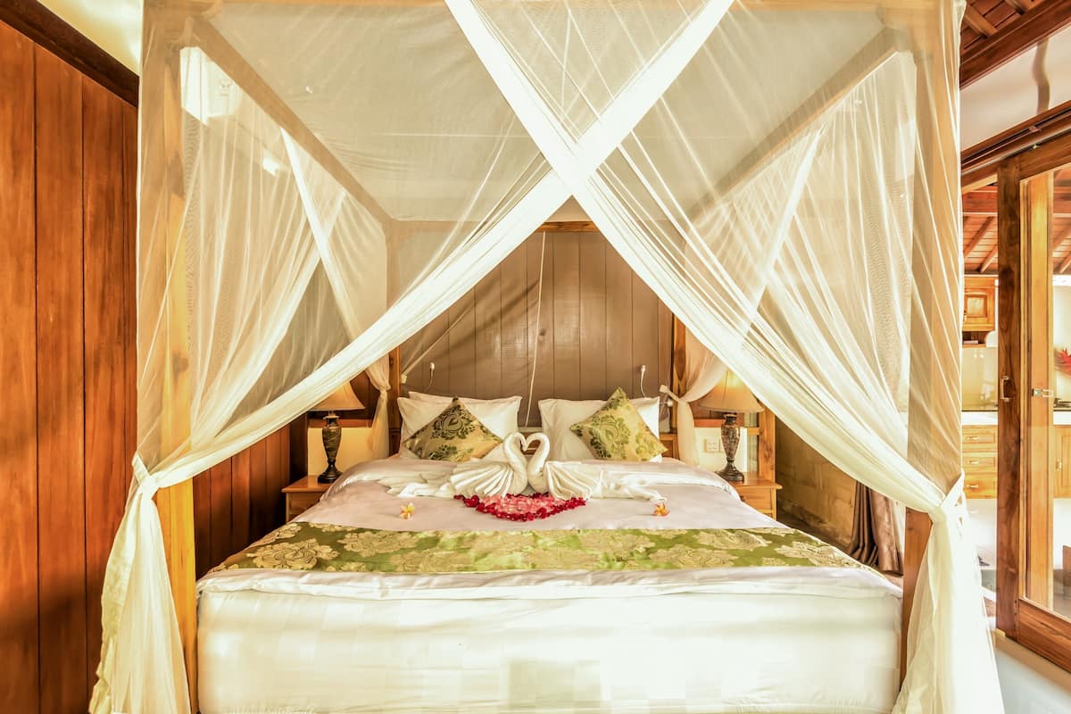 A four-poster canopy bed with a decorative swan centerpiece, wooden paneling, and a nightstand with a lamp.