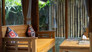 A wooden bench with colorful cushions, a small table with books, and a bamboo fence in the background. - Naja Private Villa (Ubud)