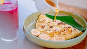 A person pouring a liquid from a small white cup into a bowl with sliced bananas on a green leaf. - Sekembang Ubud Villa (Ubud)