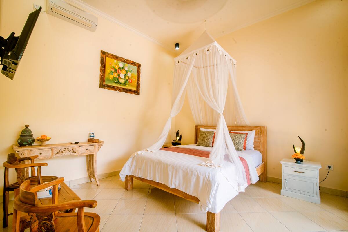 A bedroom with a four-poster bed, a desk with a chair, a nightstand, and a wall-mounted air conditioner.