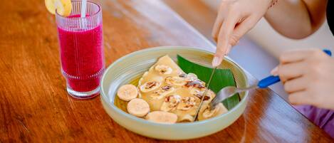 A person eating a banana dish with a side of red drink on a wooden table.
