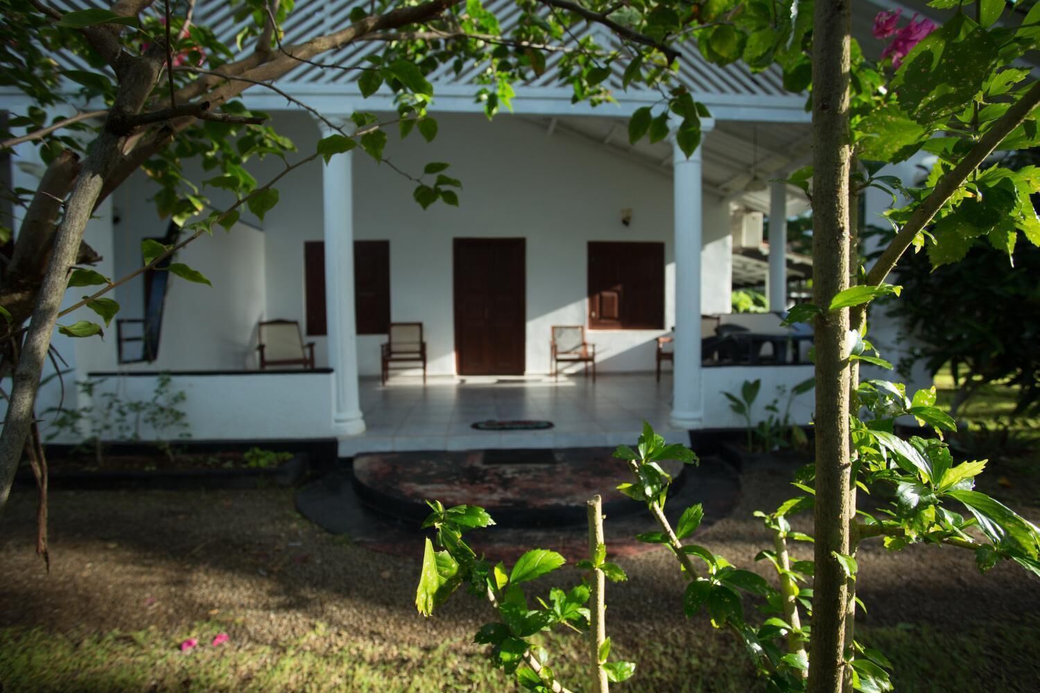 A white building with a covered porch, several chairs, and a small garden area.