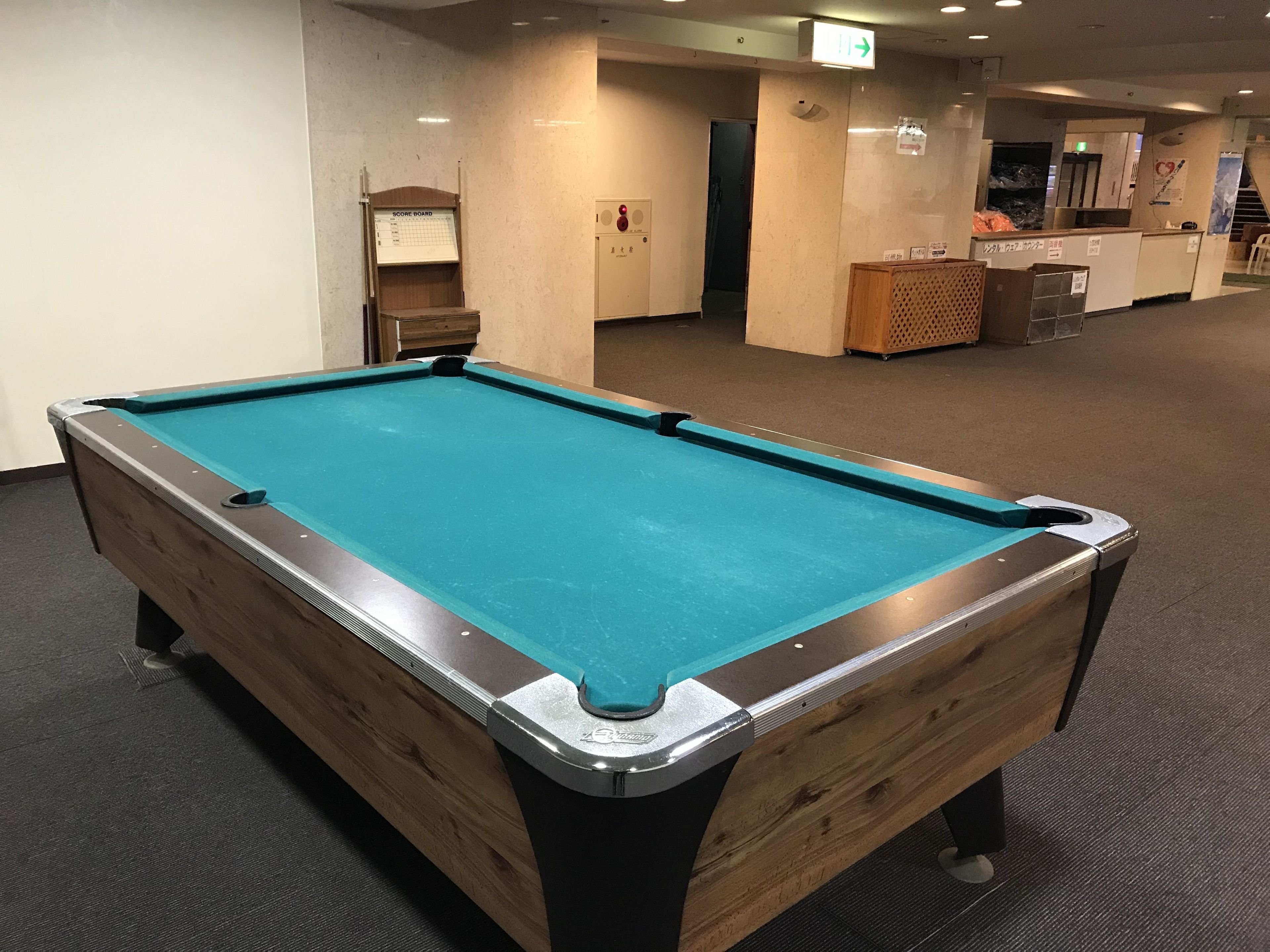 A pool table in a room with a wooden cabinet and a score board.
