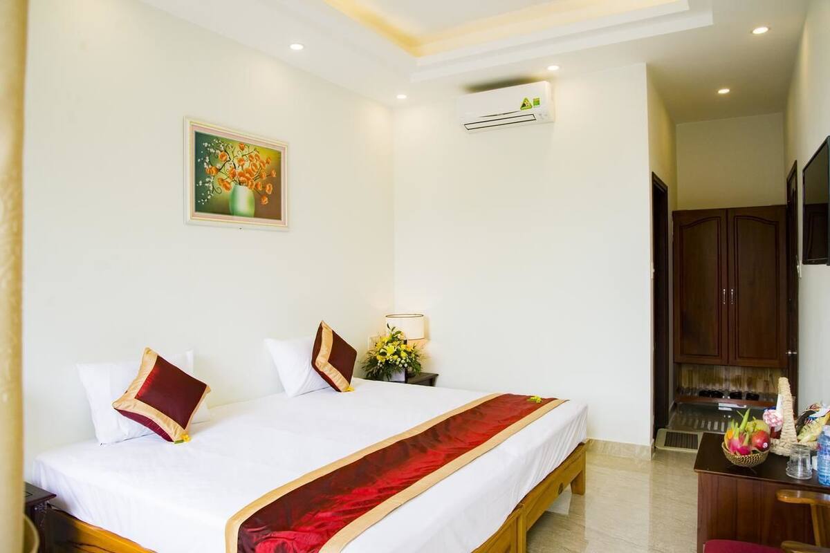 A hotel room with a bed, a nightstand with a lamp, a wall-mounted air conditioner, and a painting.