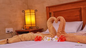 A neatly made bed with a towel arranged in a heart shape, accompanied by red and white flowers, and a wooden headboard. - Niyagala Lodge (Sigiriya)