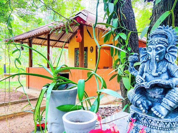 Una cabaña rústica con techo de paja, rodeada de exuberante follaje y una estatua decorativa de un elefante.