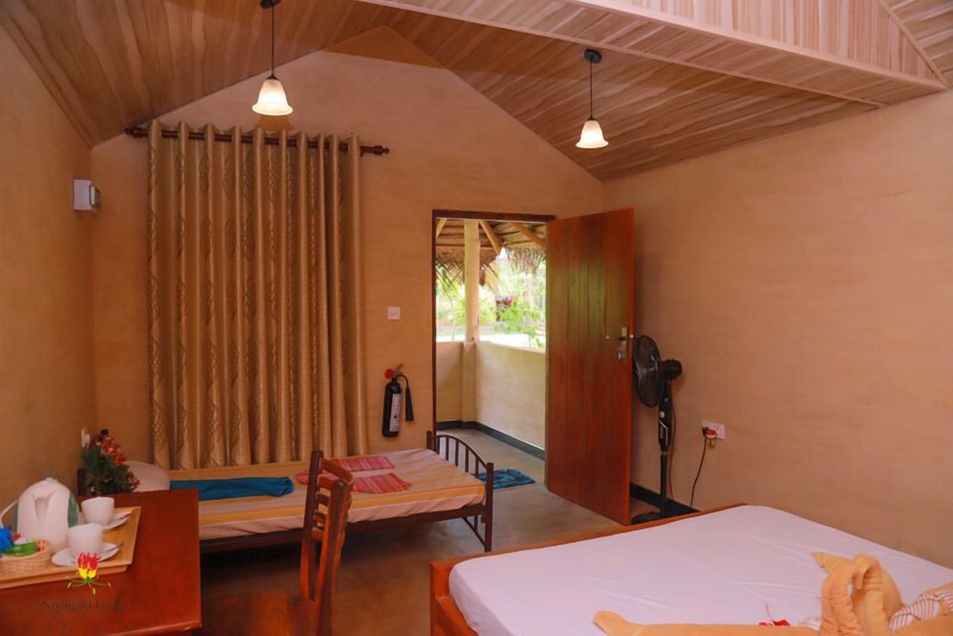 Una habitación acogedora con una cama, un escritorio con silla, un ventilador y una ventana con cortinas.