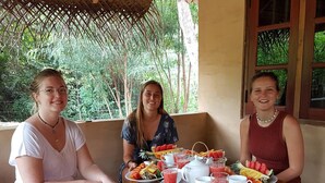 Three people seated at a wooden table with a variety of fruits and beverages. - Niyagala Lodge (Sigiriya)