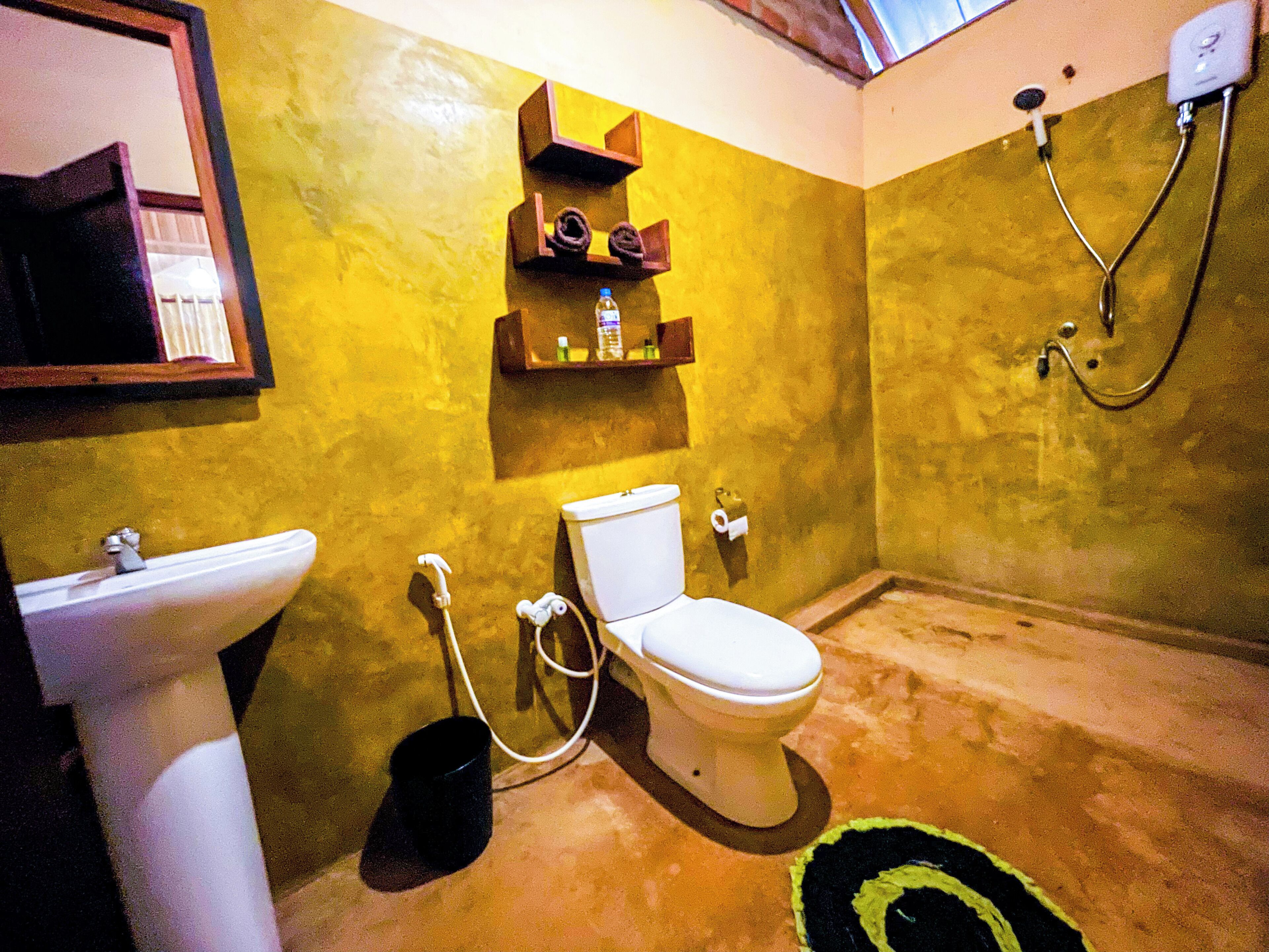 A bathroom with a toilet, sink, and shower. There are shelves above the toilet with toiletries.