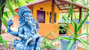 A statue of a deity in a garden setting with a small building in the background. - Niyagala Lodge (Sigiriya)