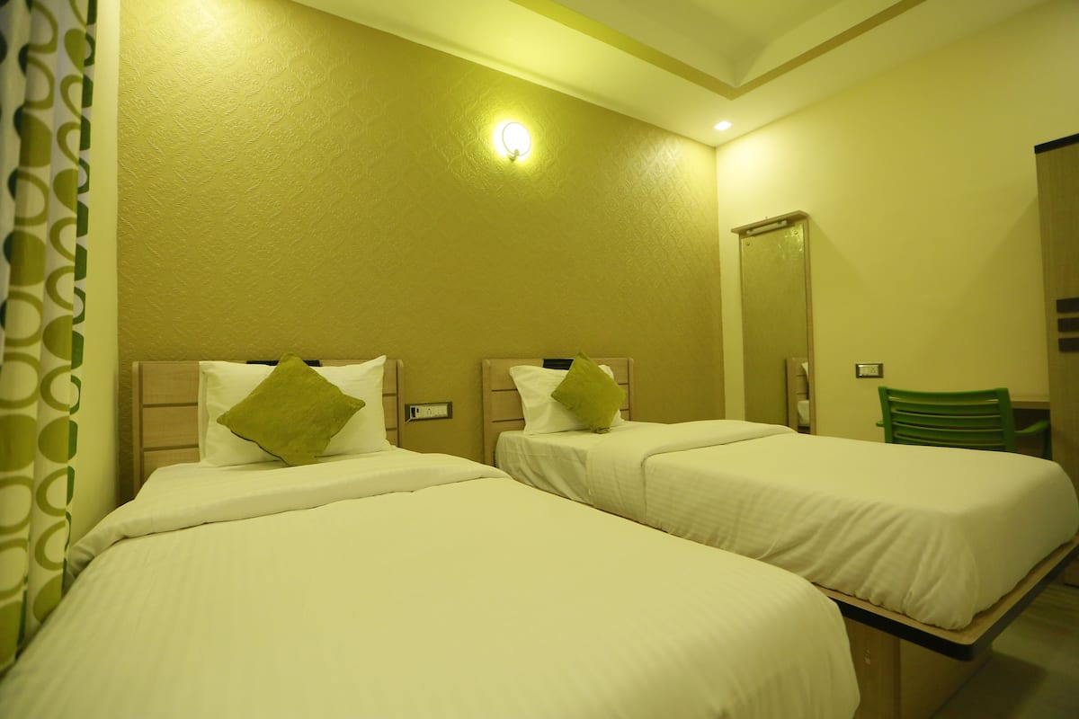 A hotel room with two single beds, a green chair, and a mirror on the wall.