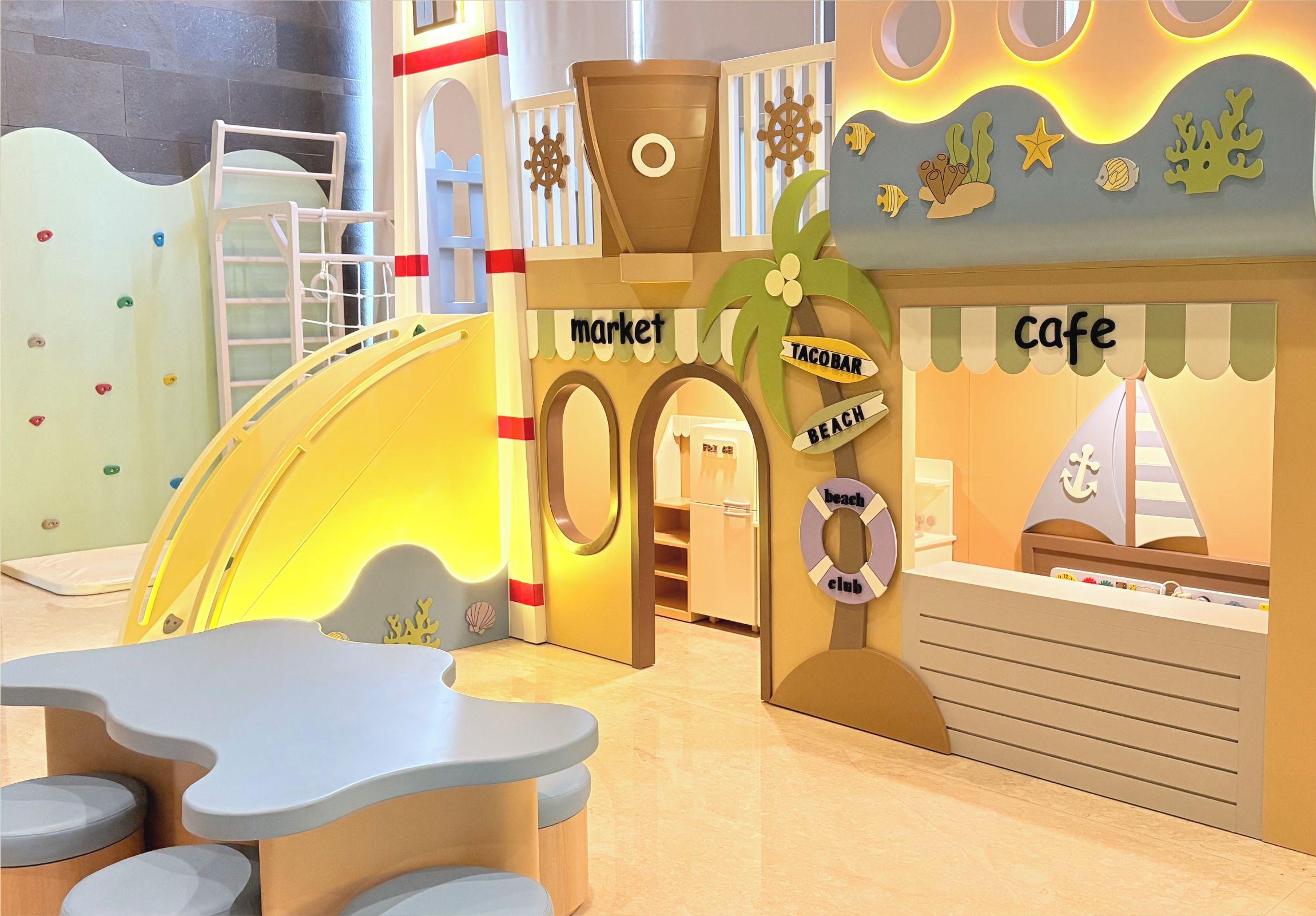 Ein Kinderspielbereich mit einer Kletterwand, einem Marktstand und einem Café.