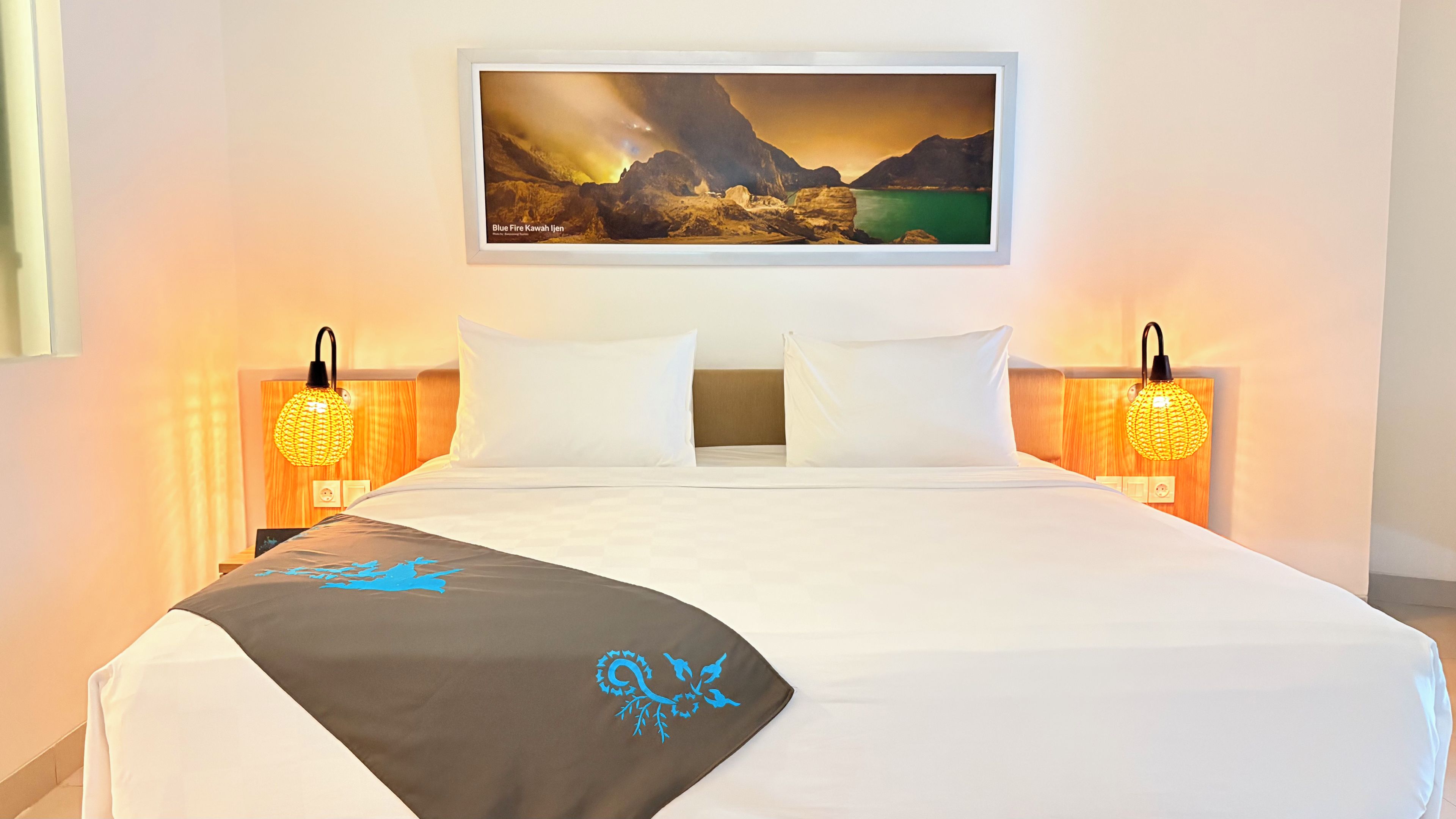 A hotel room with a bed, two bedside lamps, a framed picture on the wall, and a decorative throw blanket.