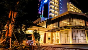 Un hôtel moderne à l’architecture imposante, avec plusieurs étages, une entrée abritée et une façade bien éclairée.