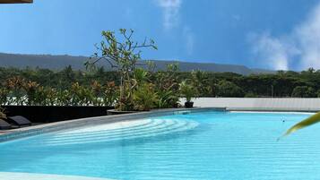 Una piscina con agua azul cristalina, rodeada de plantas tropicales y vistas a montañas distantes.