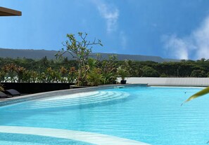 Une piscine à l’eau cristalline, entourée de plantes tropicales et offrant une vue sur des montagnes lointaines.