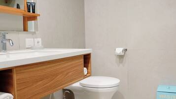 Un baño moderno con lavamanos blanco, tocador de madera, inodoro y un cubo de basura azul.