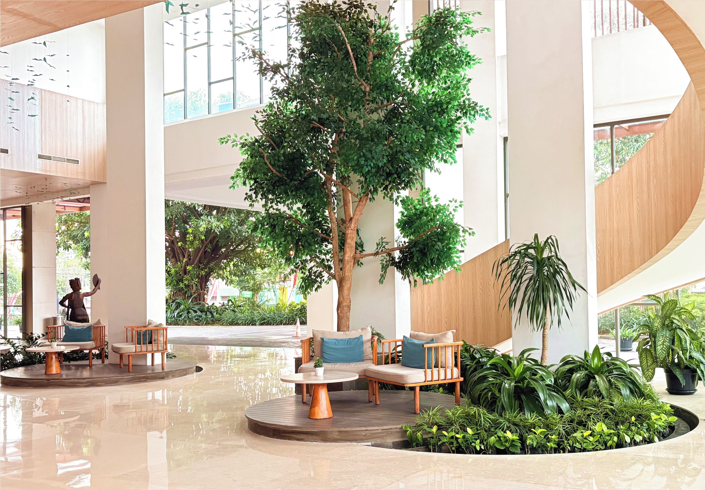 Un amplio espacio interior con un gran árbol artificial, arreglos de asientos y una fuente de agua.