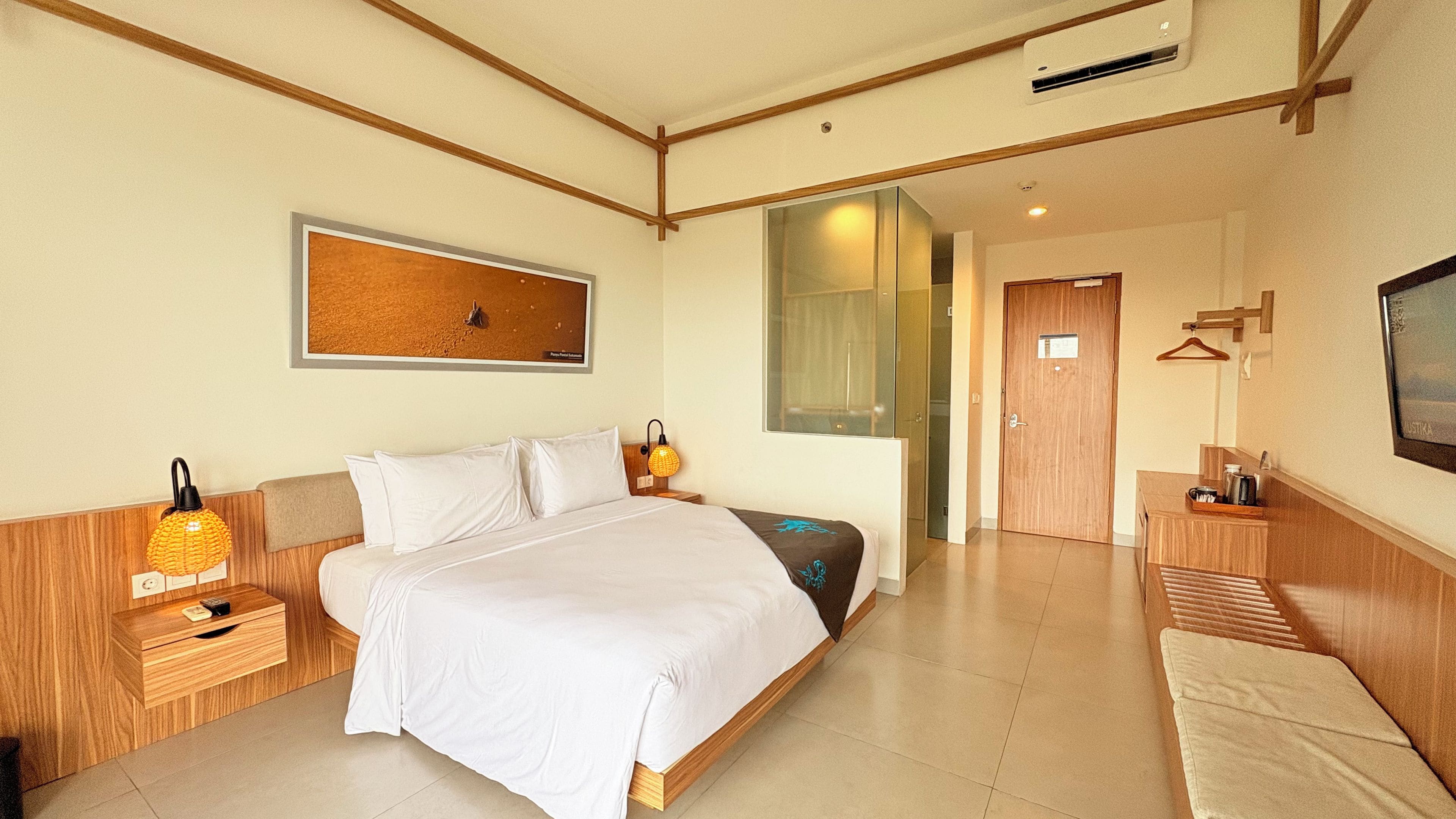 A hotel room with a bed, bedside tables, a wall-mounted TV, and a door leading to another room.