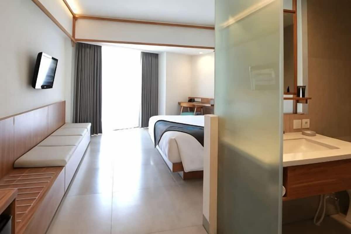 Hotelkamer met een bed, zithoek, televisie, badkamer met wastafel en raam met gordijnen.